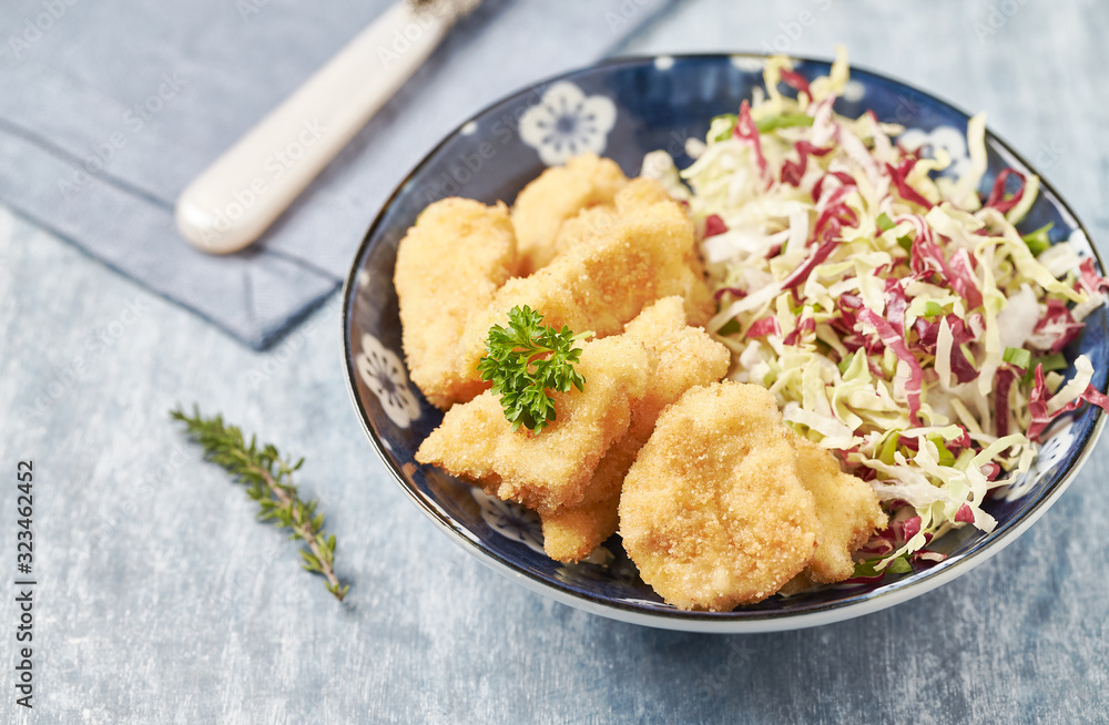 Chicken nuggets with raw salad on bright wooden background.