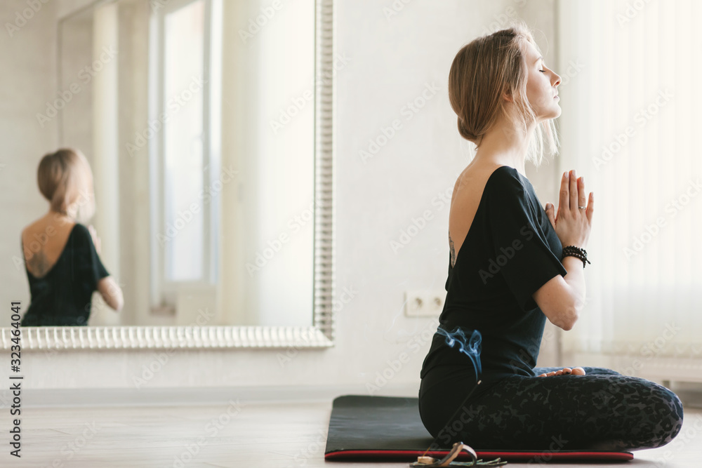 Young woman doing stretching exercise by mirror in bright yoga class room Young woman doing stretching exercise by mirror in bright yoga class room