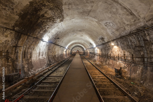 Fototapeta Naklejka Na Ścianę i Meble -  A dimly lit subway railway tunnel with an illuminated utility platform tunnel. A red light is lit in front.