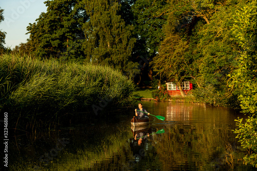 Ein Mann paddelt am Frühen Morgen in einem Kanu auf einem Fluss im Grünen