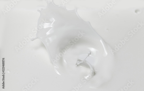Fresh milk pouring making a crown splash in a milk pool. Top view, isolated on grey-white background.