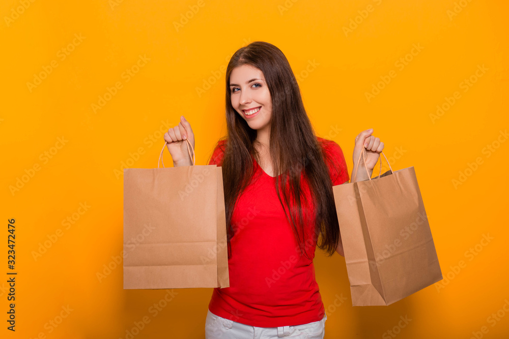 Portrait of a cheerful, happy, young woman with paper bags in hands standing on a yellow background. Shopping, discount day, black friday. Portrait of a cheerful, happy, young woman with paper bags in hands standing on a yellow background. Shopping, discount day, black friday.
