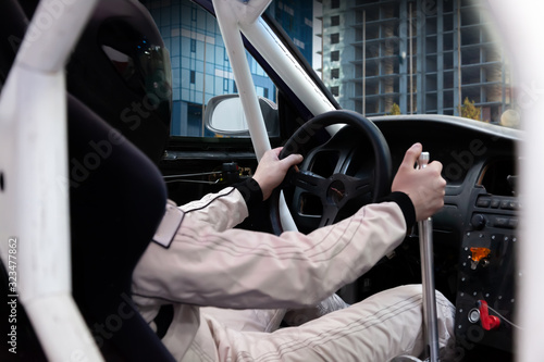 A professional racer in a black helmet and a white homologated suit sits in the sports seat of a left-hand drive car with a roll cage for drifting and racing during race and training. photo