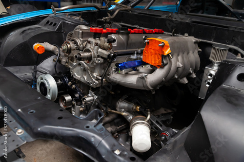 Powerful tuned gasoline engine with a turbocharger and a charger in the engine compartment of the car with an open hood in a car repair and improvement workshop.