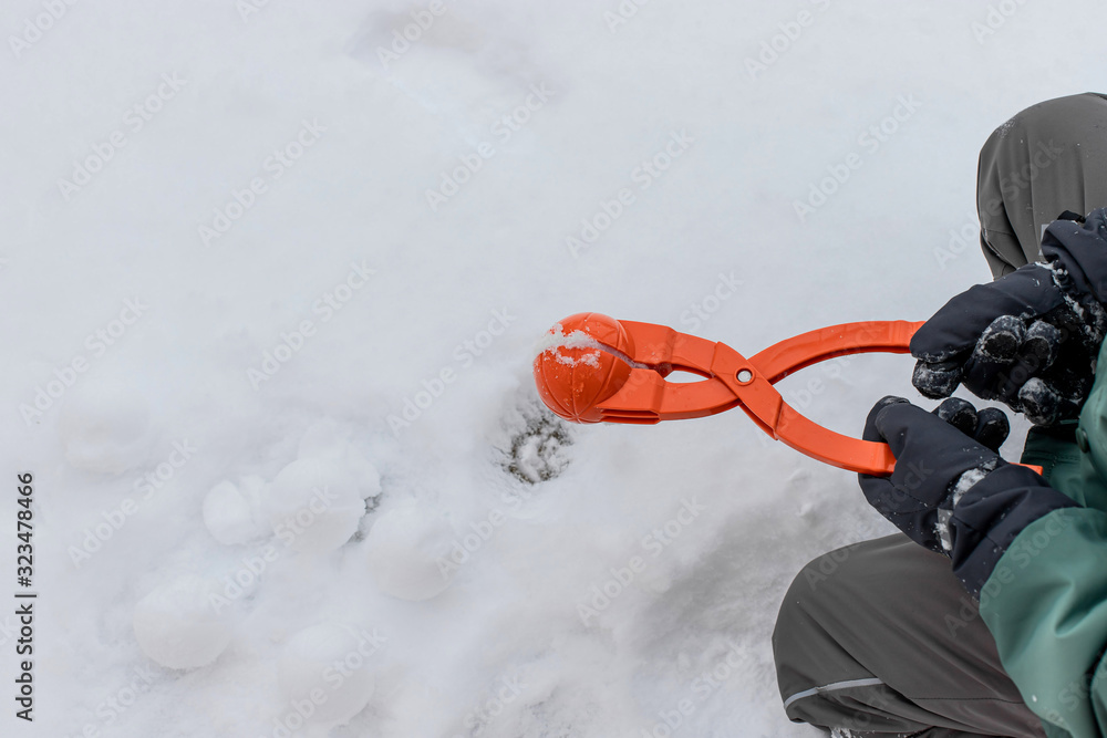 child in ski gloves holds a device for making snowballs. winter outdoor entertainment. copy space