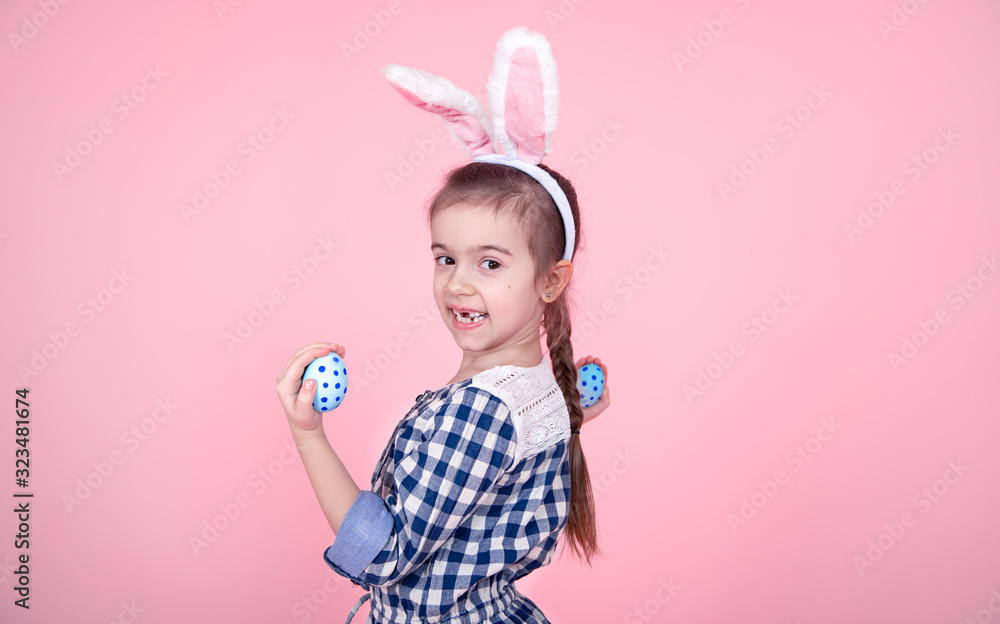Portrait of a cute little girl with Easter eggs on a pink background.