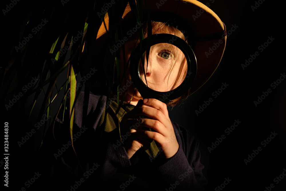 little girl with a short haircut, in a hat, through a magnifying glass  looks at the green leaves of a flower in the jungle Stock Photo | Adobe  Stock