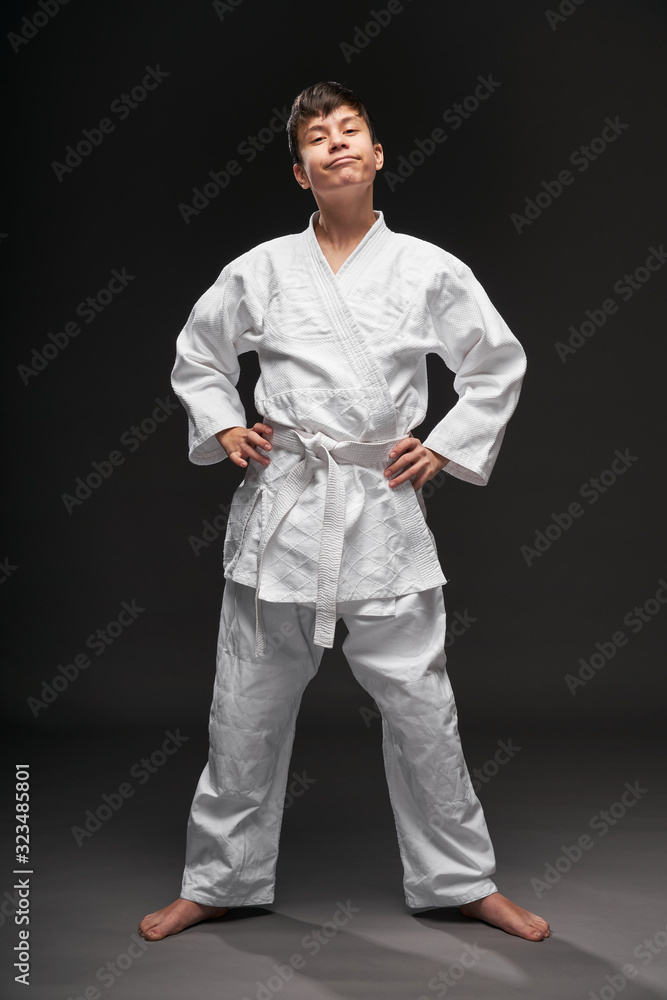 a teenager dressed in martial arts clothing poses on a dark gray background, a sports concept a teenager dressed in martial arts clothing poses on a dark gray background, a sports concept
