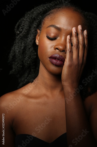 Portrait of a young beautiful African woman with thick black curly hair on an black background. The woman puts her hand over her eye