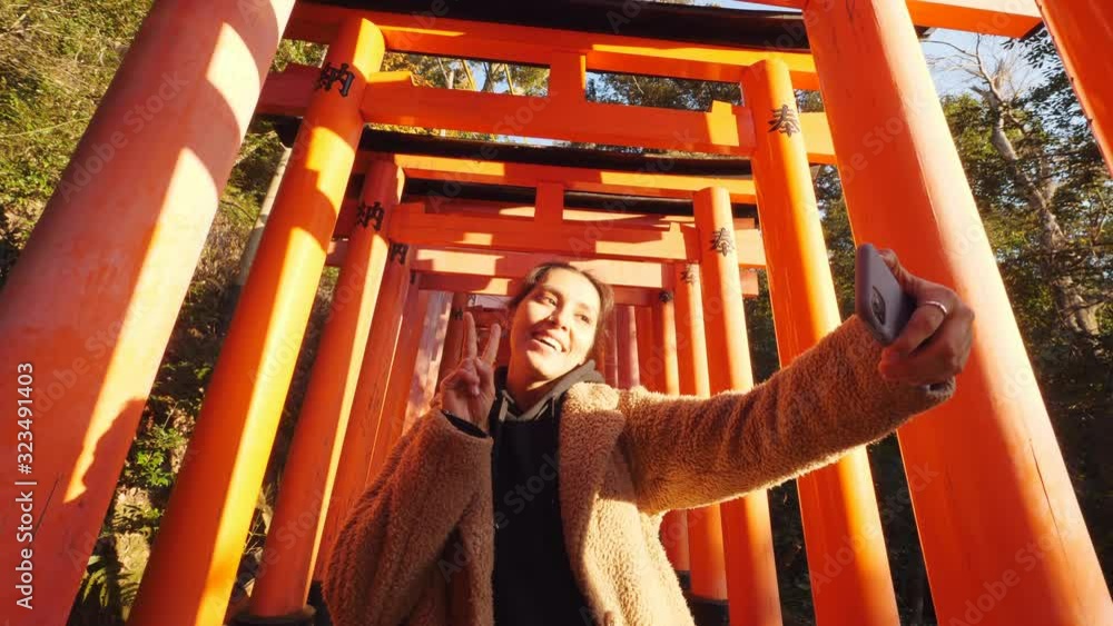 Young Woman Taking Selfie In Front Of Traditional Japanese Torii Gates With Her Smartphone. 4K Tourism Concept Footage. 6 DEC 2019 - Fushimi Inari Shrine, Kyoto, Japan. Young Woman Taking Selfie In Front Of Traditional Japanese Torii Gates With Her Smartphone. 4K Tourism Concept Footage. 6 DEC 2019 - Fushimi Inari Shrine, Kyoto, Japan.