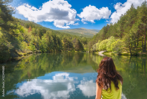 Young woman enjoys a beautiful mirrored mountain lake in the forest during a clear sky day