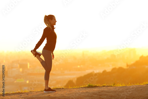 Vászonkép Runner woman stretching leg in city outskirts at sunset