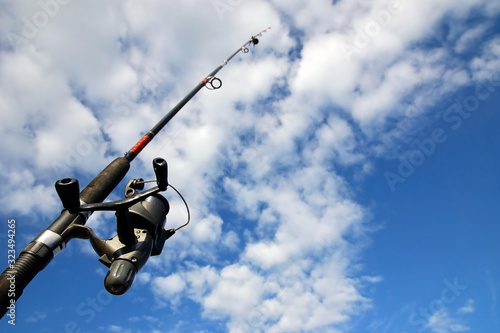 Spinning fishing rod against blue sky and clouds. Sport fishing, hobby, leisure and vacation concept