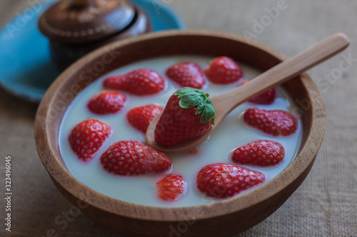 Strawberries with oat milk on a wooden bowl with a wooden spoon and another in the background on a blue plate