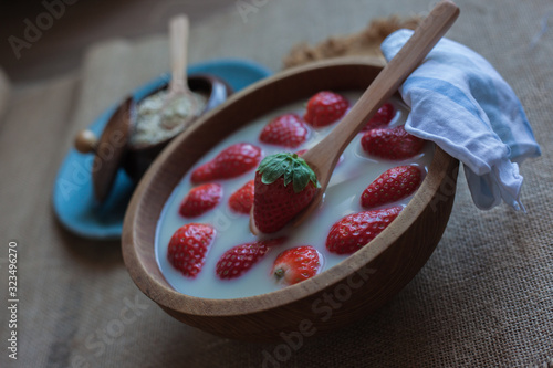 Strawberries with oat milk in a wooden bowl with a wooden spoon and a scarf and another in the background on a blue plate