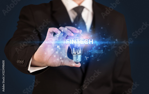 Businessman holding light bulb with FINTECH inscription, innovative technology concept