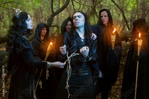 Young woman witch conjures over a man. Around them are people in black with torches.