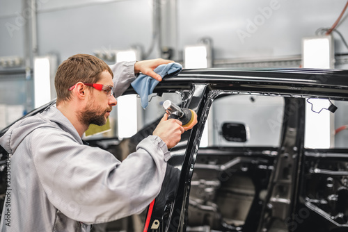 Employee in the shop painting the car body polishes painted body parts