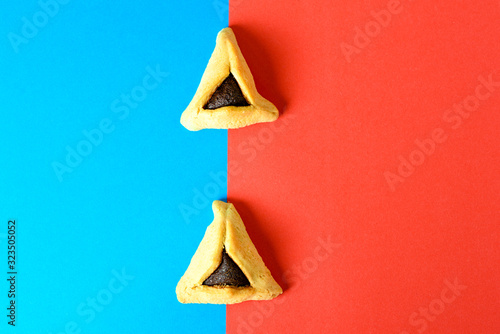 Purim holiday concept. Creative arrangement of Hamantash on red and blue paper background. Hamantaschen triangular pastries also called Haman's pockets or Oznei Haman-Haman's ears. photo