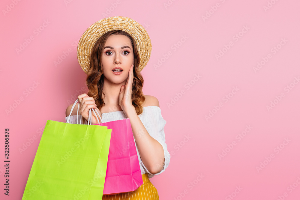 Shocked caucasian girl in a straw hat and white dress holds shopping bags in hands isolated on a pink background, copy space. Surprised, excited girl makes online shopping, web banner, sale concept Shocked caucasian girl in a straw hat and white dress holds shopping bags in hands isolated on a pink background, copy space. Surprised, excited girl makes online shopping, web banner, sale concept