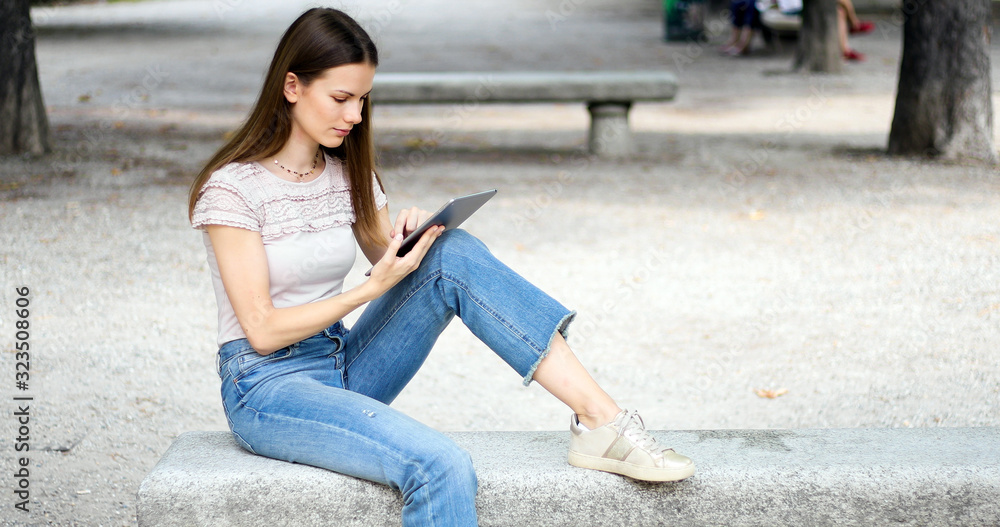 Fototapeta premium Girl with tablet sitting on a park bench