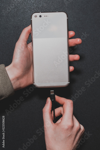 close-up of female hands that plug a smartphone into charging on a black background