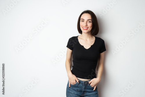 Fotografie Happy beautiful girl holds hands in pockets and smiles with snow-white teeth at the camera