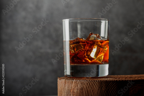 Whiskey with ice or brandy in a glass on a rustic background. Whiskey with ice in a glass. Whiskey or brandy. Selective focus.