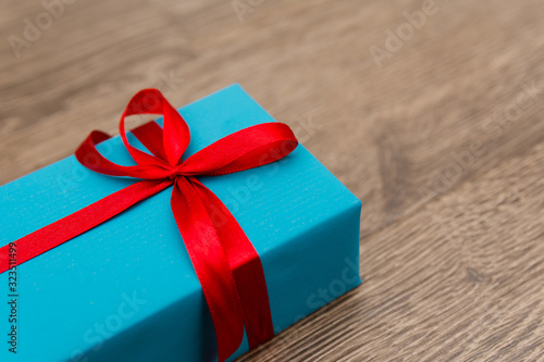 A smartphone in a blue gift box with a red ribbon lies on a wooden background. A gift for a holiday in a beautiful package. A sign of attention to a loved ones on their birthday. Selective focus