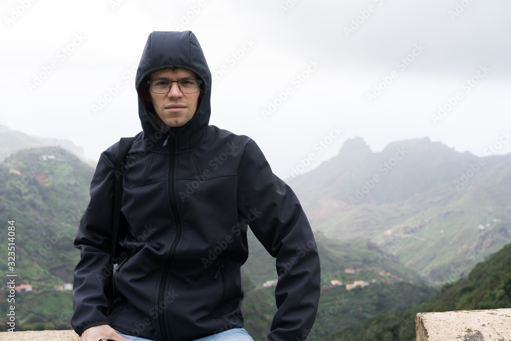 Man traveler in blue raincoat enjoying hiking in the beautiful scary mystic rainforest trees in Anaga national park on Tenerife island, Spain. Rain, fog, silence in old forest Man traveler in blue raincoat enjoying hiking in the beautiful scary mystic rainforest trees in Anaga national park on Tenerife island, Spain. Rain, fog, silence in old forest