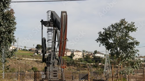 Industrial urban landscape. La Brea Inglewood in Los Angeles. Well pump jack operating behind the fence. Drilling rig extract crude oil. Oil mining machine with working piston. Oil and gas industry.