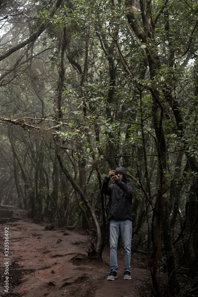 Man traveler in blue raincoat enjoying hiking in the beautiful scary mystic rainforest trees in Anaga national park on Tenerife island, Spain. Rain, fog, silence in old forest Man traveler in blue raincoat enjoying hiking in the beautiful scary mystic rainforest trees in Anaga national park on Tenerife island, Spain. Rain, fog, silence in old forest