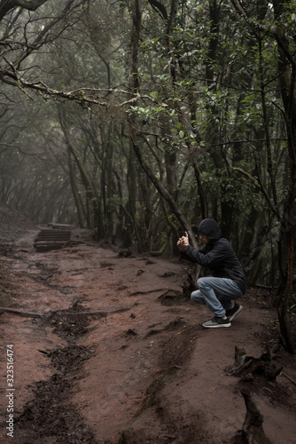 Man traveler in blue raincoat enjoying hiking in the beautiful scary mystic rainforest trees in Anaga national park on Tenerife island, Spain. Rain, fog, silence in old forest