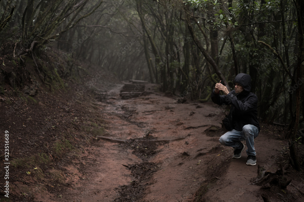 Man traveler in blue raincoat enjoying hiking in the beautiful scary mystic rainforest trees in Anaga national park on Tenerife island, Spain. Rain, fog, silence in old forest Man traveler in blue raincoat enjoying hiking in the beautiful scary mystic rainforest trees in Anaga national park on Tenerife island, Spain. Rain, fog, silence in old forest