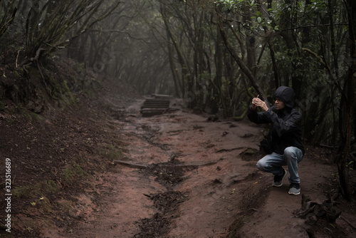 Man traveler in blue raincoat enjoying hiking in the beautiful scary mystic rainforest trees in Anaga national park on Tenerife island, Spain. Rain, fog, silence in old forest