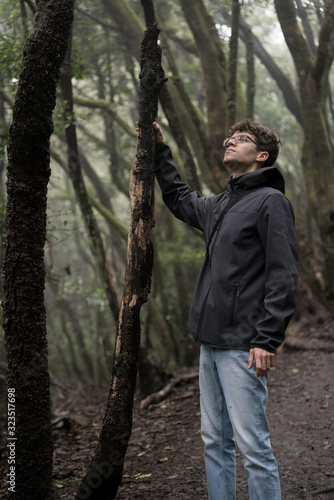 Man traveler in blue raincoat enjoying hiking in the beautiful scary mystic rainforest trees in Anaga national park on Tenerife island, Spain. Rain, fog, silence in old forest © Anna