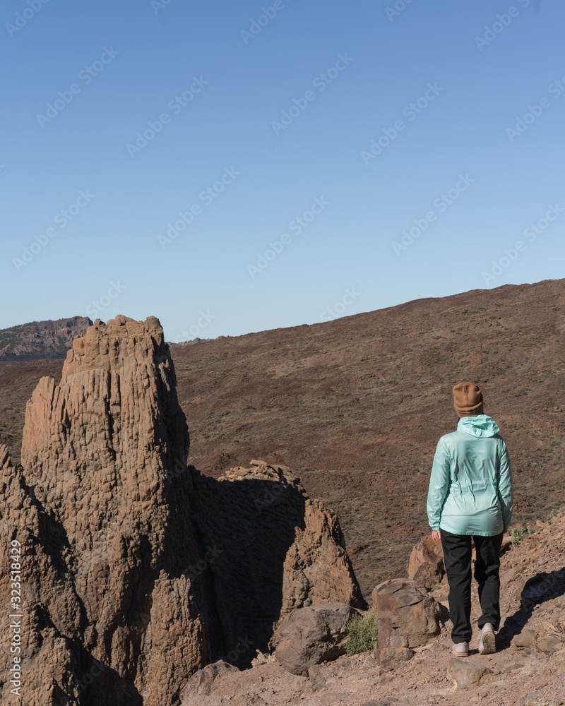 Woman in bright blue jacket the beautiful volcanic valley with mountains on the background during. Winter traveling on Tenerife island, Spain Woman in bright blue jacket the beautiful volcanic valley with mountains on the background during. Winter traveling on Tenerife island, Spain