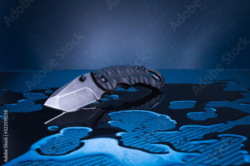 Knife with a black blade and a handle on a blue background. Knife on the water. Reflection of a knife in the water. photo