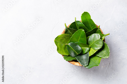 Kaffir lime Leaves in a wooden bowl on a light background. Top view. Copy space. photo