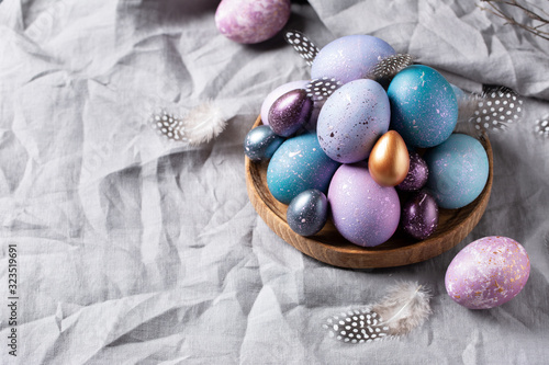 Easter. Festive bright eggs in a wooden bowl on a background of gray cotton fabric. Space for text.