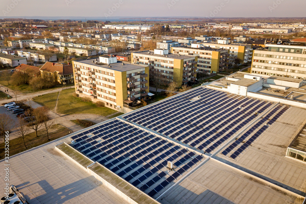 Aerial view of blue shiny solar photo voltaic panels system on commercial roof producing renewable clean energy on city landscape background. Aerial view of blue shiny solar photo voltaic panels system on commercial roof producing renewable clean energy on city landscape background.