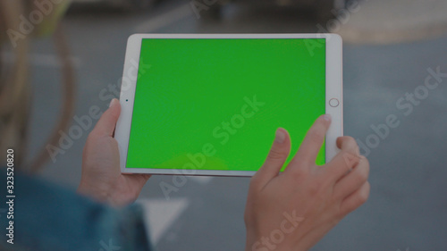Lviv, Ukraine - May 19, 2018: Close-up of girl holding vertical tablet digital computer with mock-up green display in busy city road during night time. Urban lifestyle.