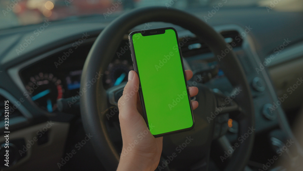 Lviv, Ukraine - May 19, 2018: Female driver sitting in the car browsing online map on vertical mock-up smartphone greenscreen searching route planning a roadtrip. Lifestyle and technology.