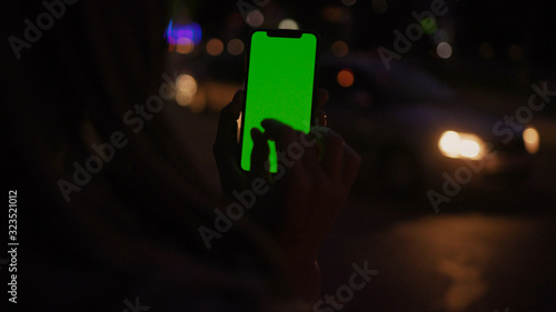 Lviv, Ukraine - May 19, 2018: Close-up of woman browsing smartphone vertical greenscreen mock-up with swipe and zoom gestures on night city background.