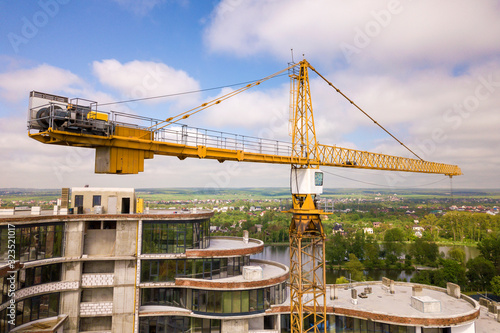 Apartment or office tall building under construction. Brick walls, glass windows, scaffolding and concrete support pillars. Tower crane on bright blue sky copy space background.