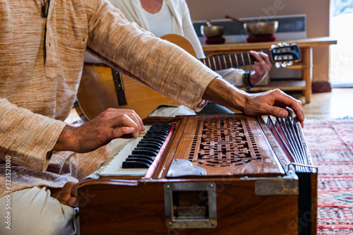 Closeup of male shaman hands playing sacred kirtan music with fingers on keys of harmonium with woman playing classical guitar in room to meditate photo