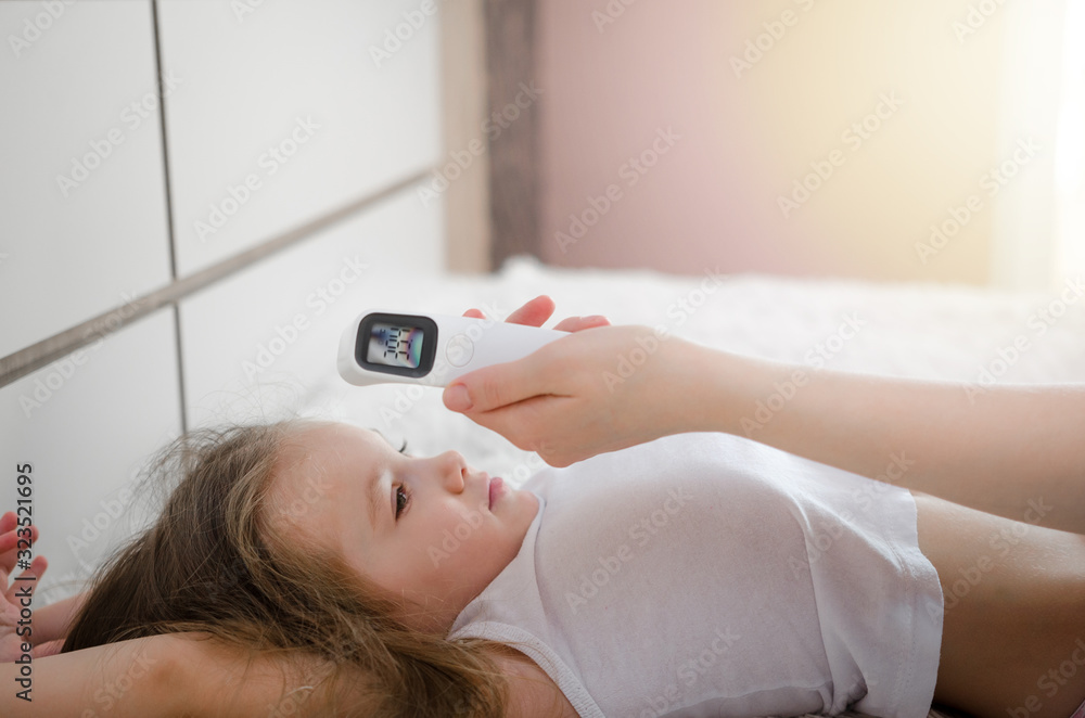 Mother takes temperature for her child with infrared thermometer at home. Mother hand holding digital infrared thermometer. Mother takes temperature for her child with infrared thermometer at home. Mother hand holding digital infrared thermometer.