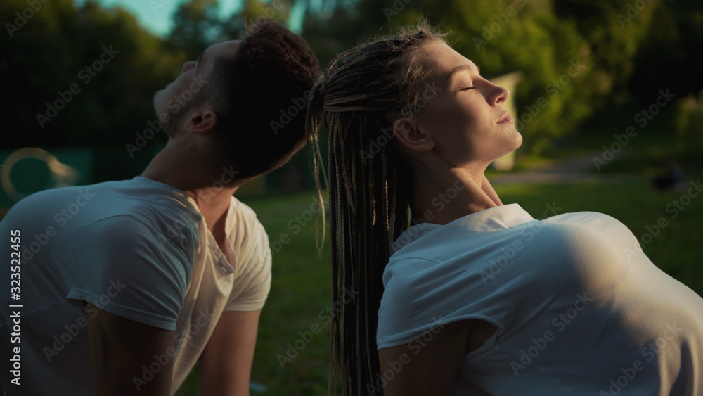 Fototapeta premium Relaxed healthy young caucasian couple meditating in bliss sitting back to back on mat practising yoga at sunset outdoors.