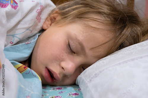 Close up of a face of pretty little child girl with slightly open mouth and scattered around hair sleeping in bed at home.