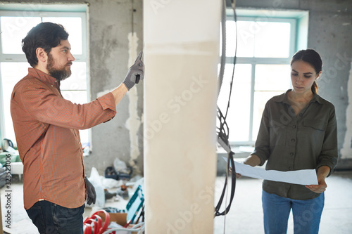 Portrait of married couple doing home renovations, man and woman separated by wall in house under construction, copy space photo